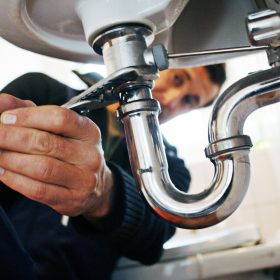 Close-up of plumber repairing sink. Male worker using tool while fixing appliance in bathroom. He is working on metallic equipment at home.